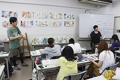 授業の様子。壁やホワイトボードに資料や作品を貼り、指差しや口頭で説明している。